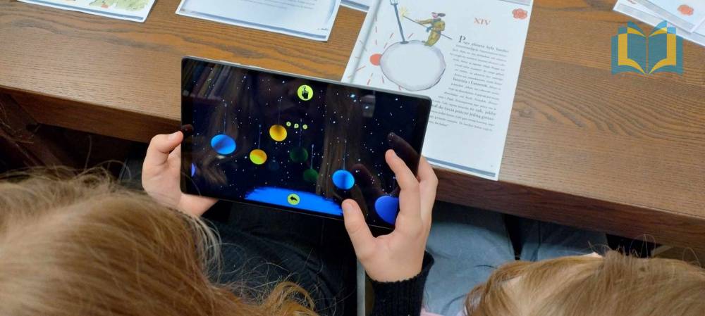 Zdjęcie: Młoda osoba trzyma w rękach tablet, za pomocą którego poznaje technologię rozszerzonej rzeczywistości. Na ekranie widoczna galaktyka i krążące planety.